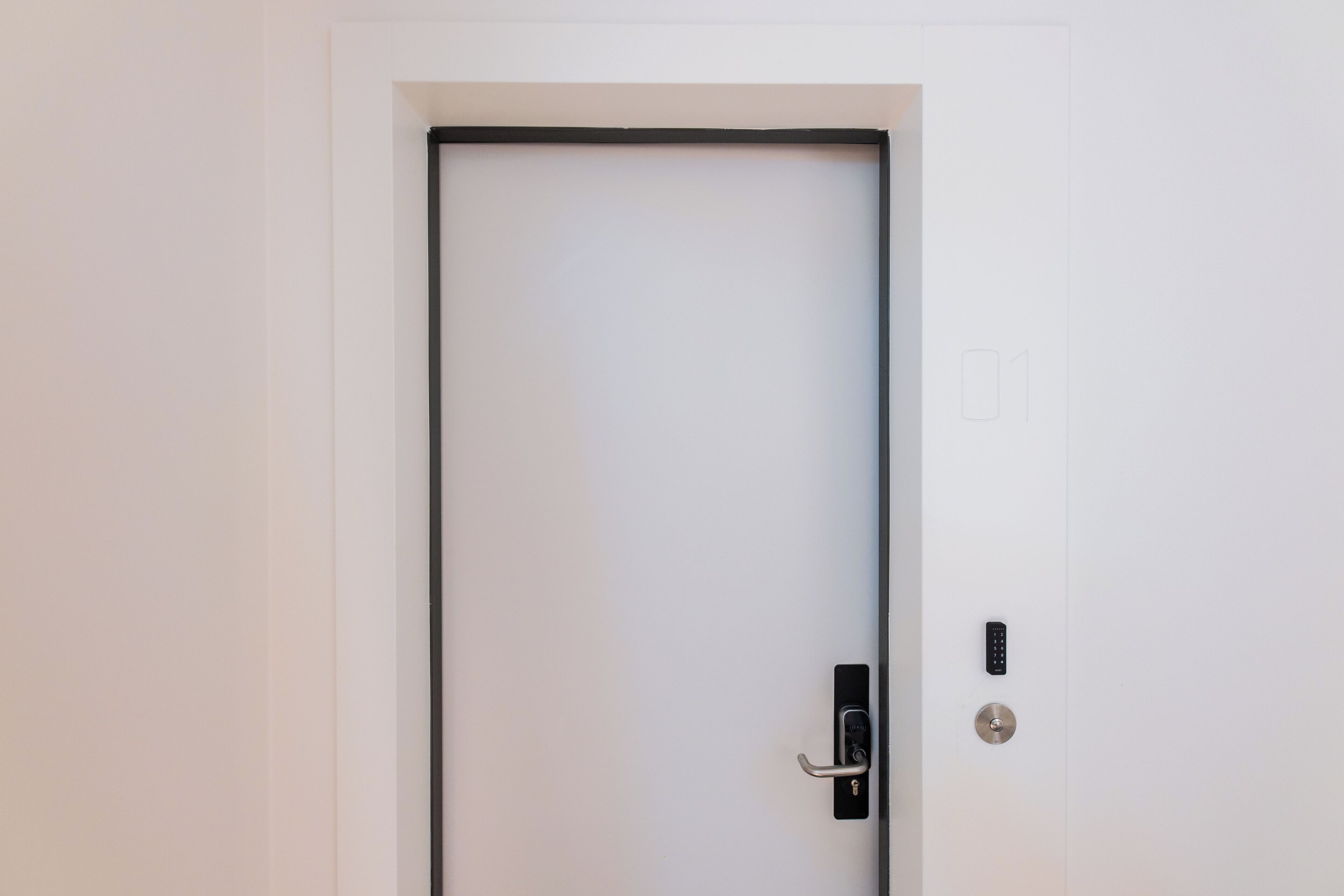 A white door with a black frame, a keyhole, and a modern electronic lock.