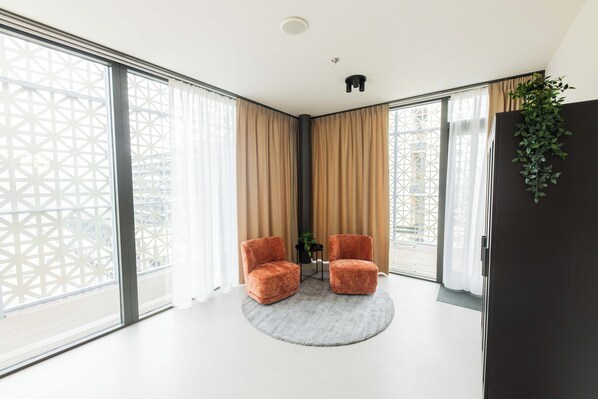 A modern room with large windows, two plush armchairs, a small table, and a potted plant.