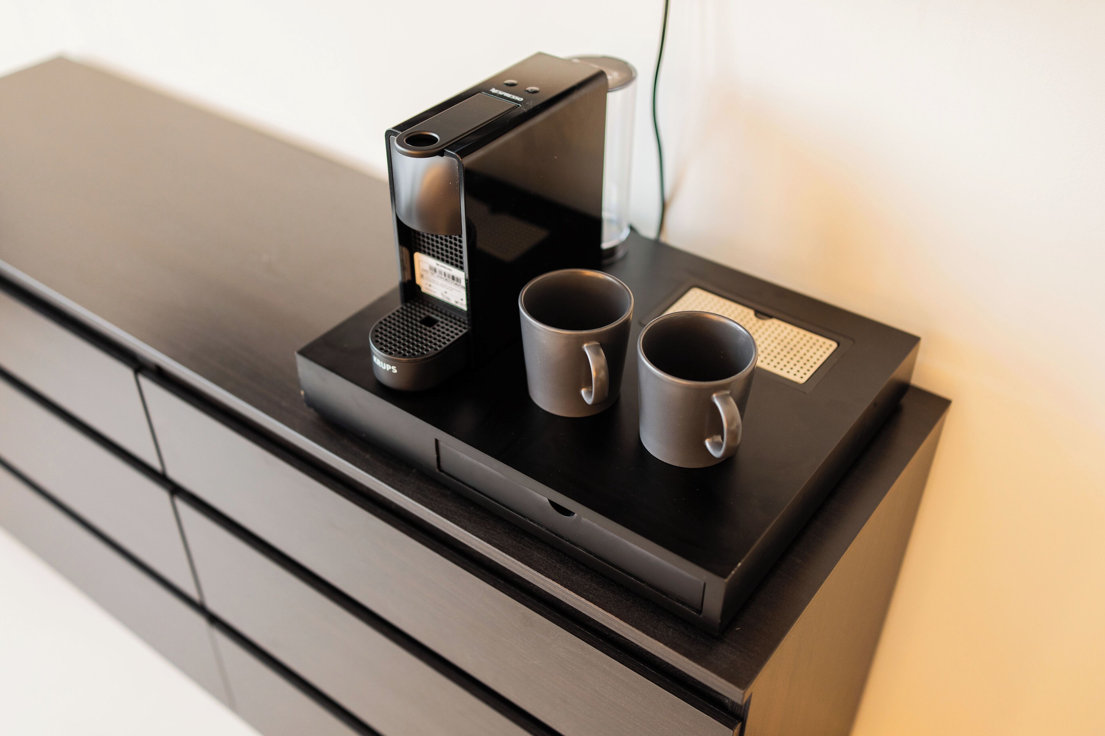 A coffee maker on a black countertop with two mugs.