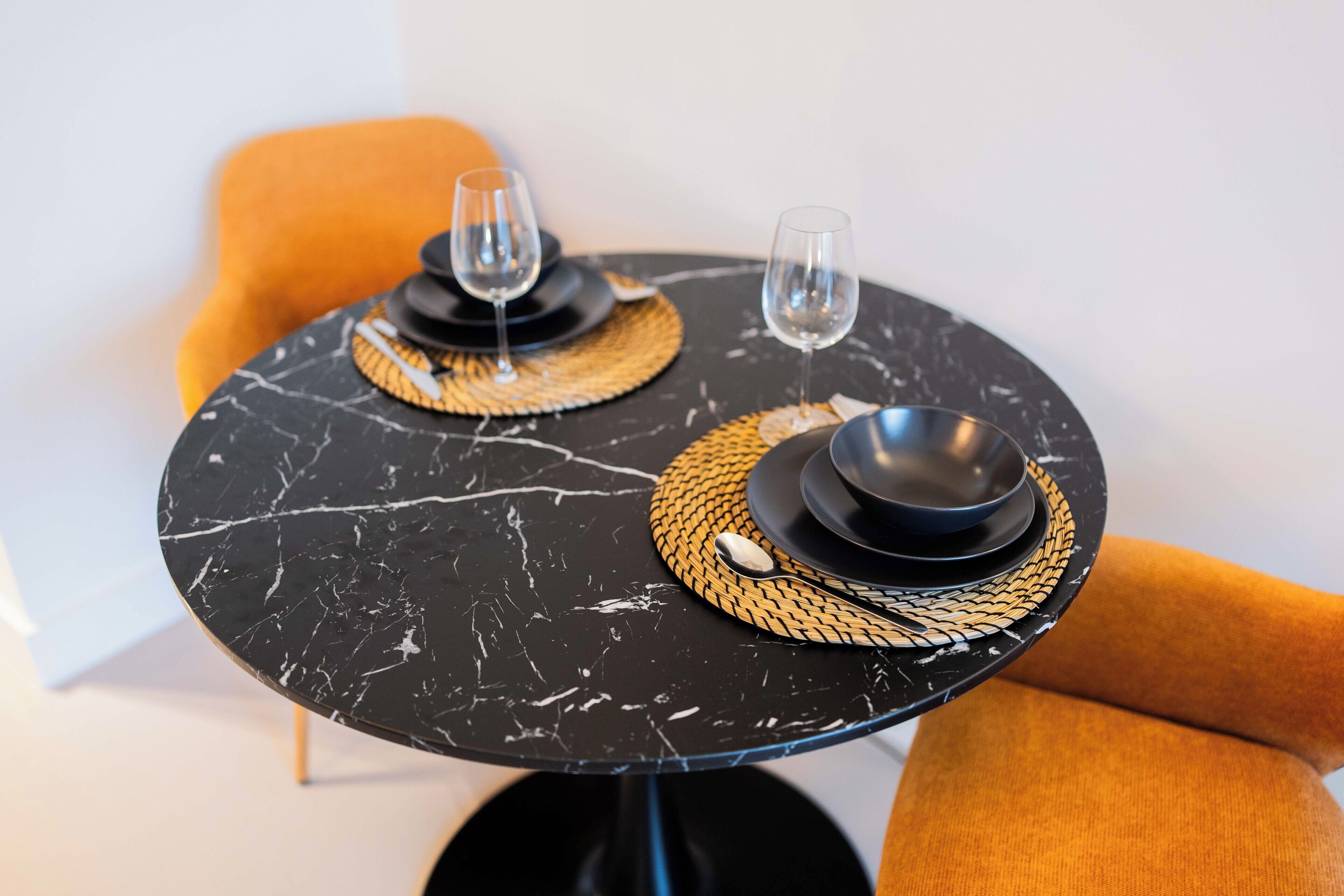 Una mesa redonda con dos platos negros, cada uno con un tapete tejido debajo.