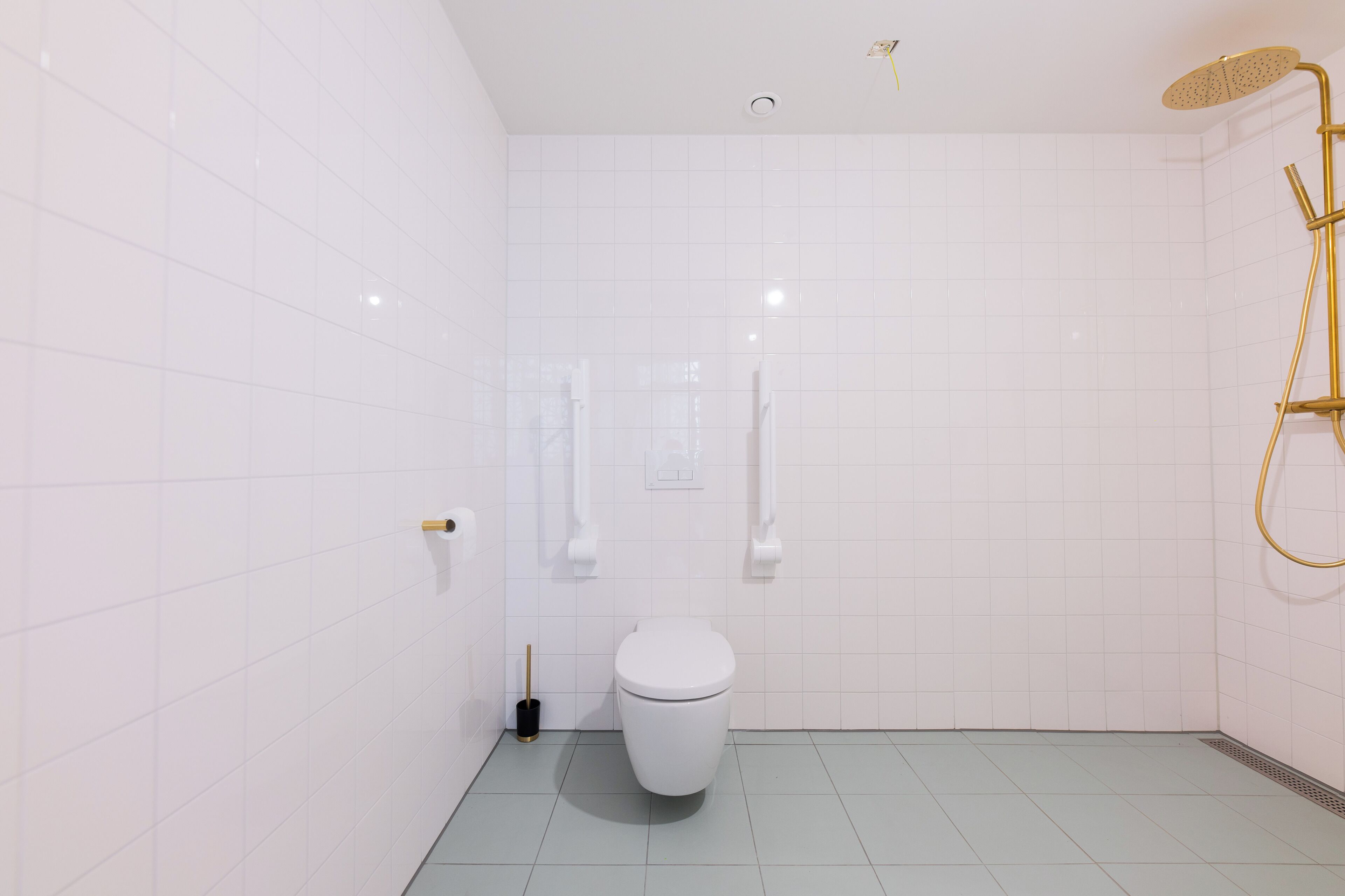 Une salle de bain moderne avec des carreaux blancs, des toilettes blanches, une pomme de douche dorée et un pommeau de douche à main.