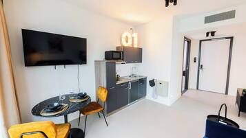 Een moderne woonkamer met een flatscreen televisie, een eethoek met een ronde tafel en stoelen, een keuken met een magnetron en een spoelbak, en een deur met het nummerbord '01'.