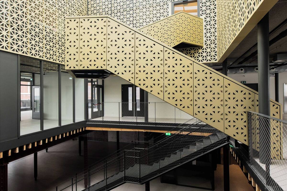 A modern interior with a central staircase, glass railings, and geometric patterned walls.