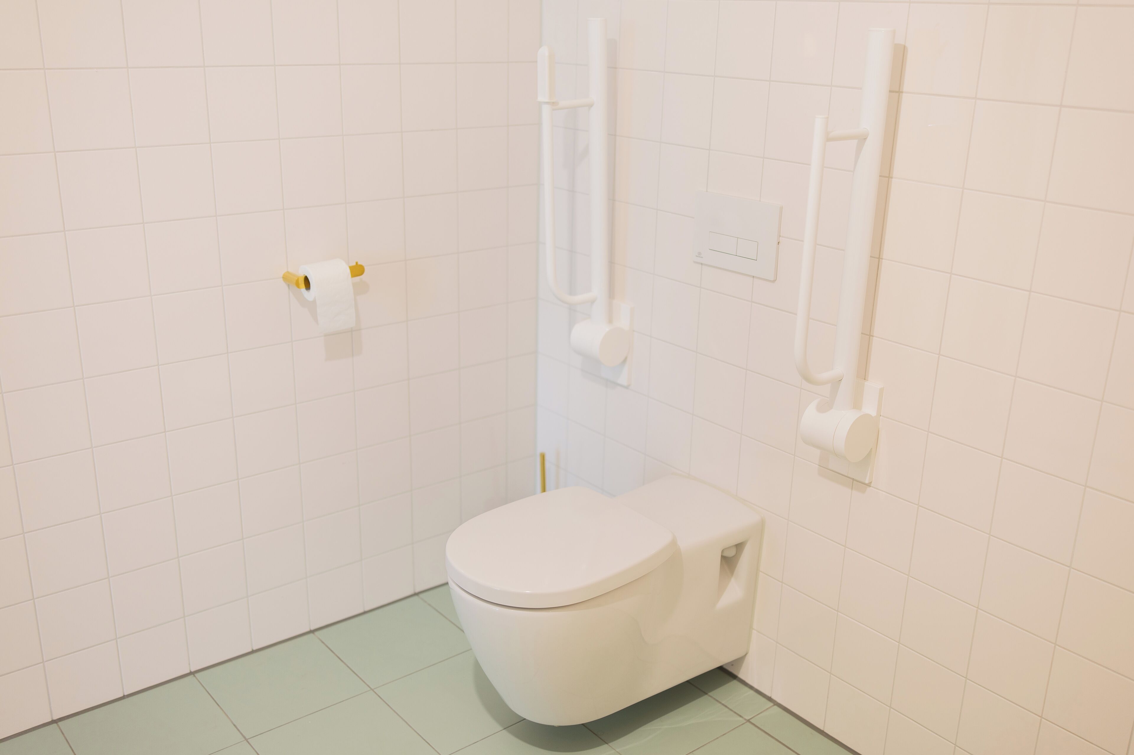 A small, white bathroom with a toilet, a toilet paper holder, and a hand dryer on the wall.