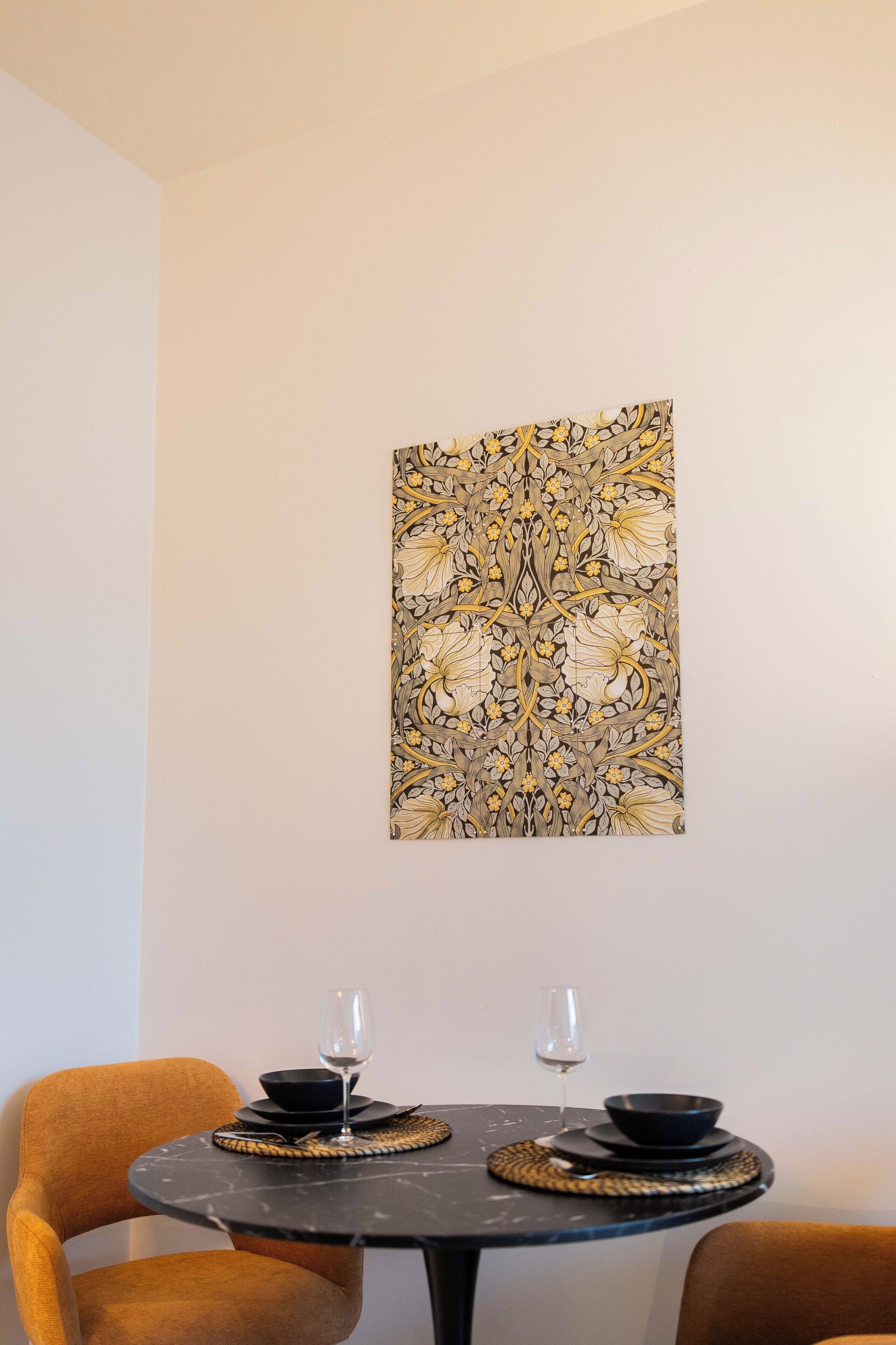 Un comedor con una mesa redonda, dos sillas y una obra de arte floral colgada en la pared.