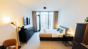 A modern hotel room with a bed, a desk, a chair, a TV, and a large window with curtains. - Alphabet Apartments Brede Hilledijk (Rotterdam)