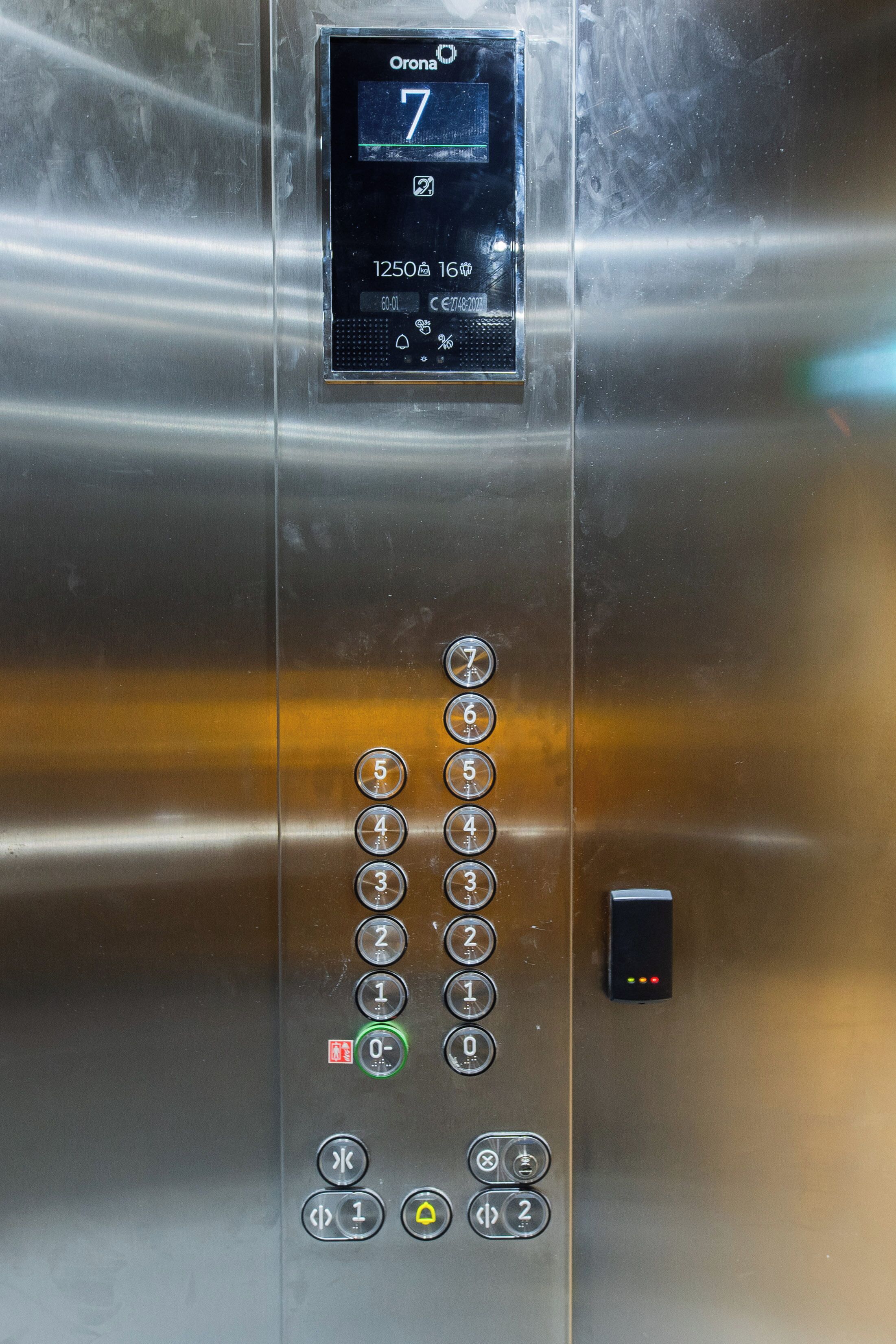 An elevator control panel with a digital display showing the floor number 7, buttons for floor selection, and emergency stop buttons.