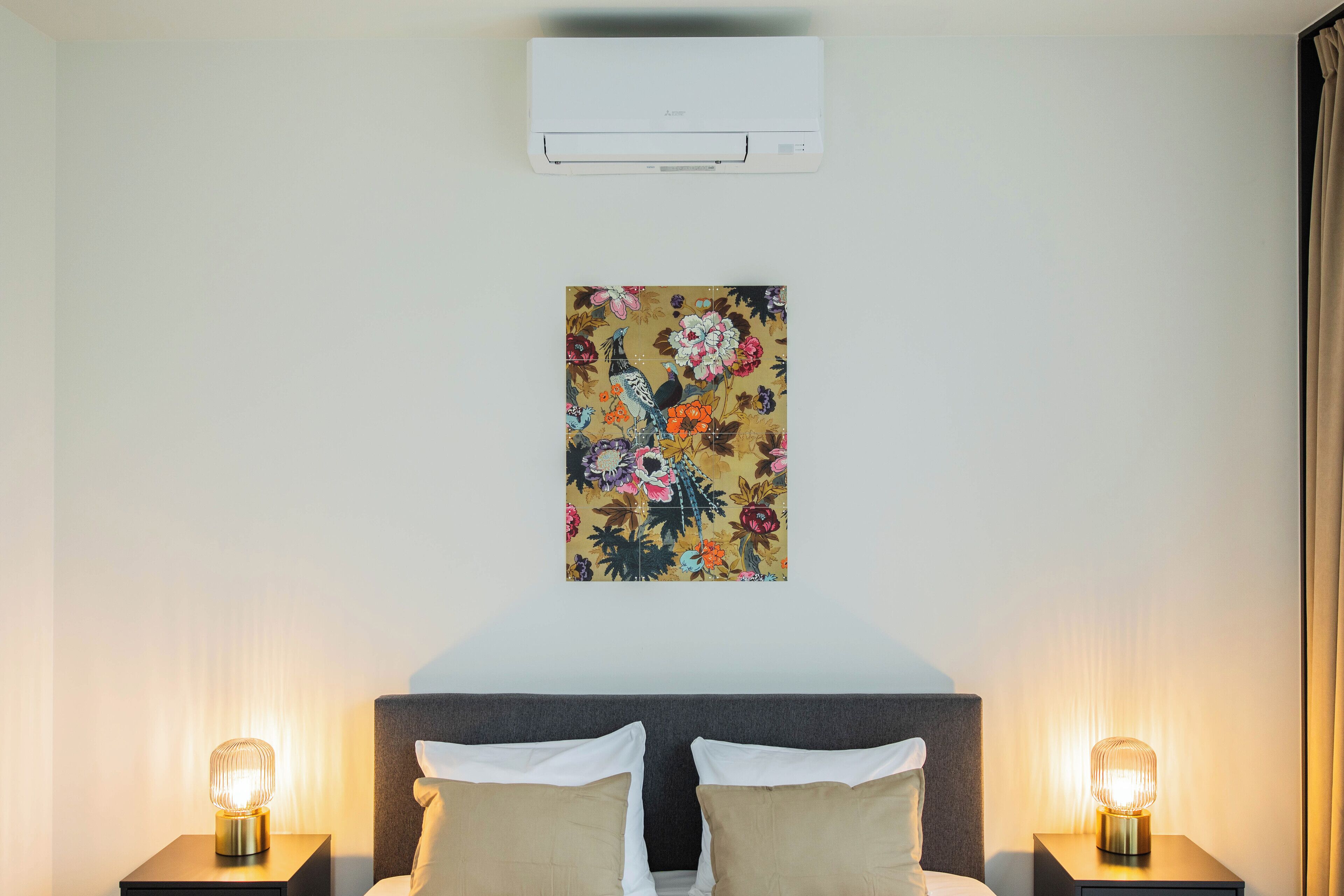 Una habitación de hotel con una cama, dos lámparas de noche, aire acondicionado y una obra de arte floral en la pared.