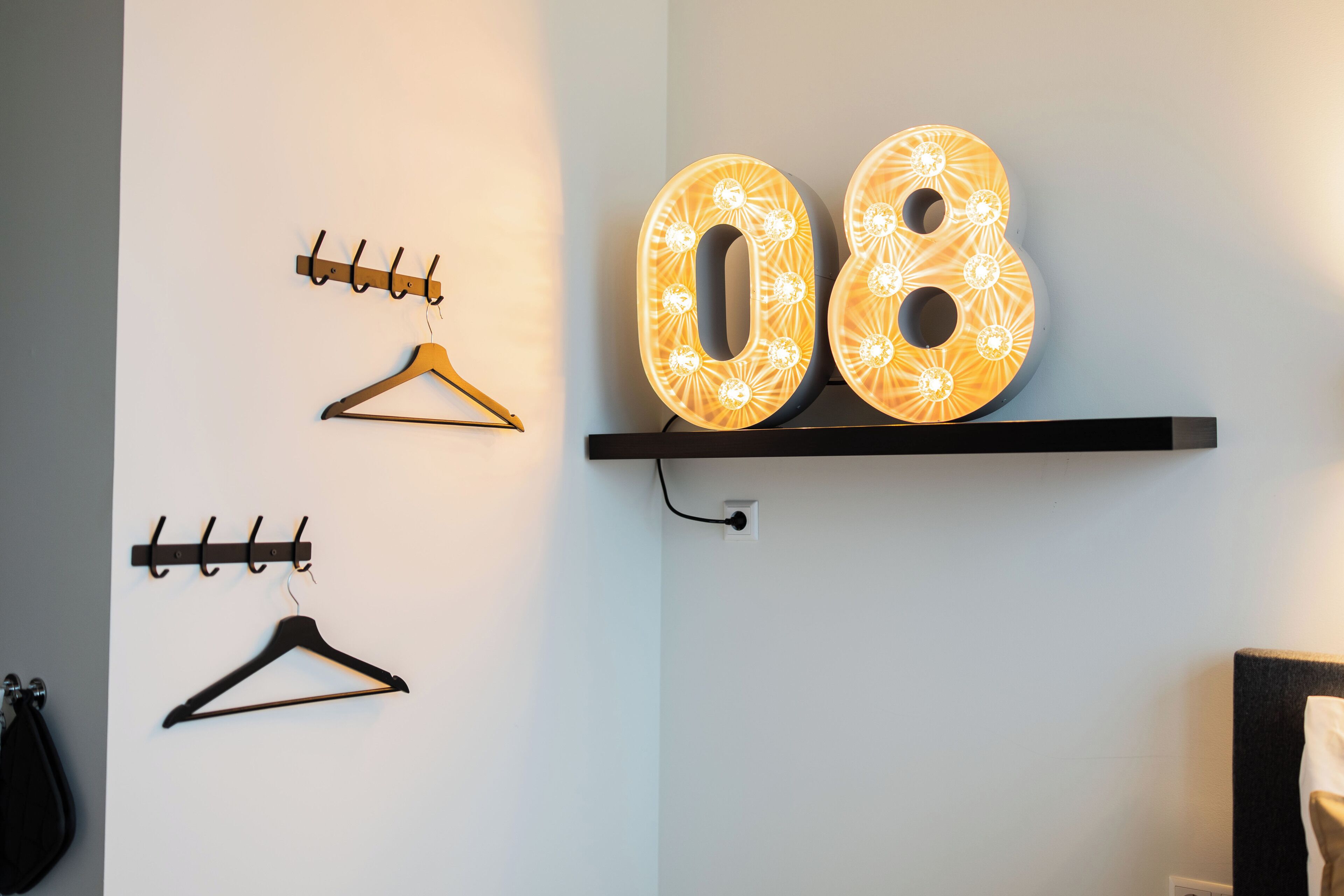 Ein an der Wand befestigter Kleiderhaken mit zwei Haken und beleuchteten Zahlen '08' auf einem Regal.