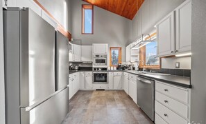 A modern kitchen with white cabinetry, stainless steel appliances, and a wooden ceiling.