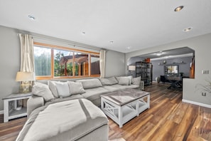 A spacious living area with a large sectional sofa, a coffee table, and a dining area with a wooden table and chairs.