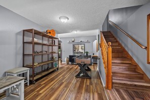 Una habitación amplia con una escalera de madera, una gran estantería y una mesa de fútbol.