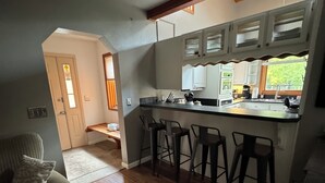 A kitchen with a central island, bar stools, and a window with a view of greenery. - COZY HILLSIDE HOME WITH A BEAUTIFUL DECK, FIRE PIT, SAUNA & PLENTY OF PARKING (Anchorage)