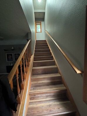 A wooden staircase with a handrail, leading to a landing with a small window. - COZY HILLSIDE HOME W BEAUTIFUL DECK, FIRE PIT, SAUNA,BACKYARD & HUGE GAME-ROOM!! (Anchorage)