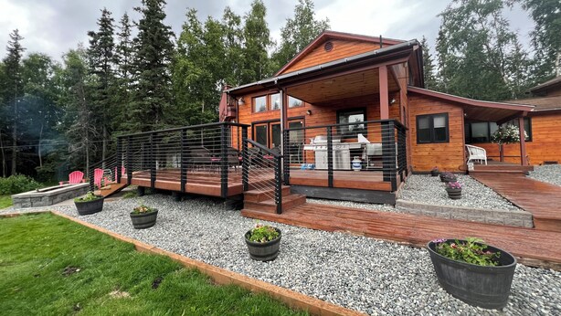 A wooden cabin with a deck, outdoor seating, and potted plants. - COZY HILLSIDE HOME WITH A BEAUTIFUL DECK, FIRE PIT, SAUNA & PLENTY OF PARKING (Anchorage)