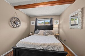 Un dormitorio con cama, mesitas de noche, ventana con cortinas, un reloj de pared y un espejo decorativo.
