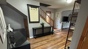 A hallway with wooden flooring, a black console table, a decorative vase, and a staircase with wooden railings. - COZY HILLSIDE HOME WITH A BEAUTIFUL DECK, FIRE PIT, SAUNA & PLENTY OF PARKING (Anchorage)