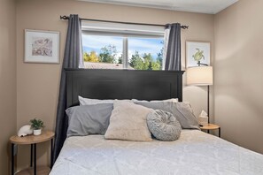 A bedroom with a bed, two bedside tables, a window with curtains, and wall art. - COZY HILLSIDE HOME W BEAUTIFUL DECK, FIRE PIT, SAUNA,BACKYARD & HUGE GAME-ROOM!! (Anchorage)