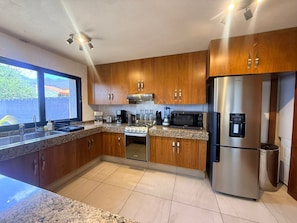 A modern kitchen with granite countertops, wooden cabinets, stainless steel appliances, and a large window.