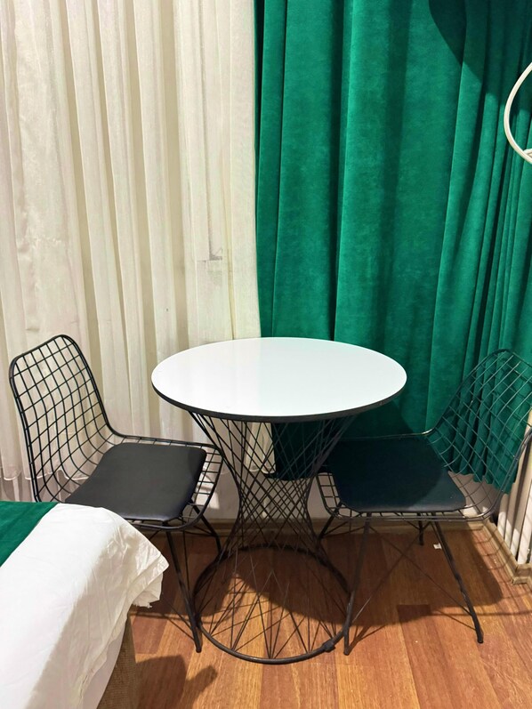 A small room with a round table and two chairs, a bed with a white cover, and green curtains. - Taksim Plaza Suite (Istanbul)
