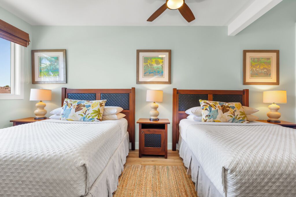 A hotel room with two beds, a ceiling fan, and framed artwork on the walls.