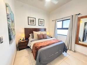 A bedroom with a bed, nightstands, a window with curtains, and framed pictures on the wall.