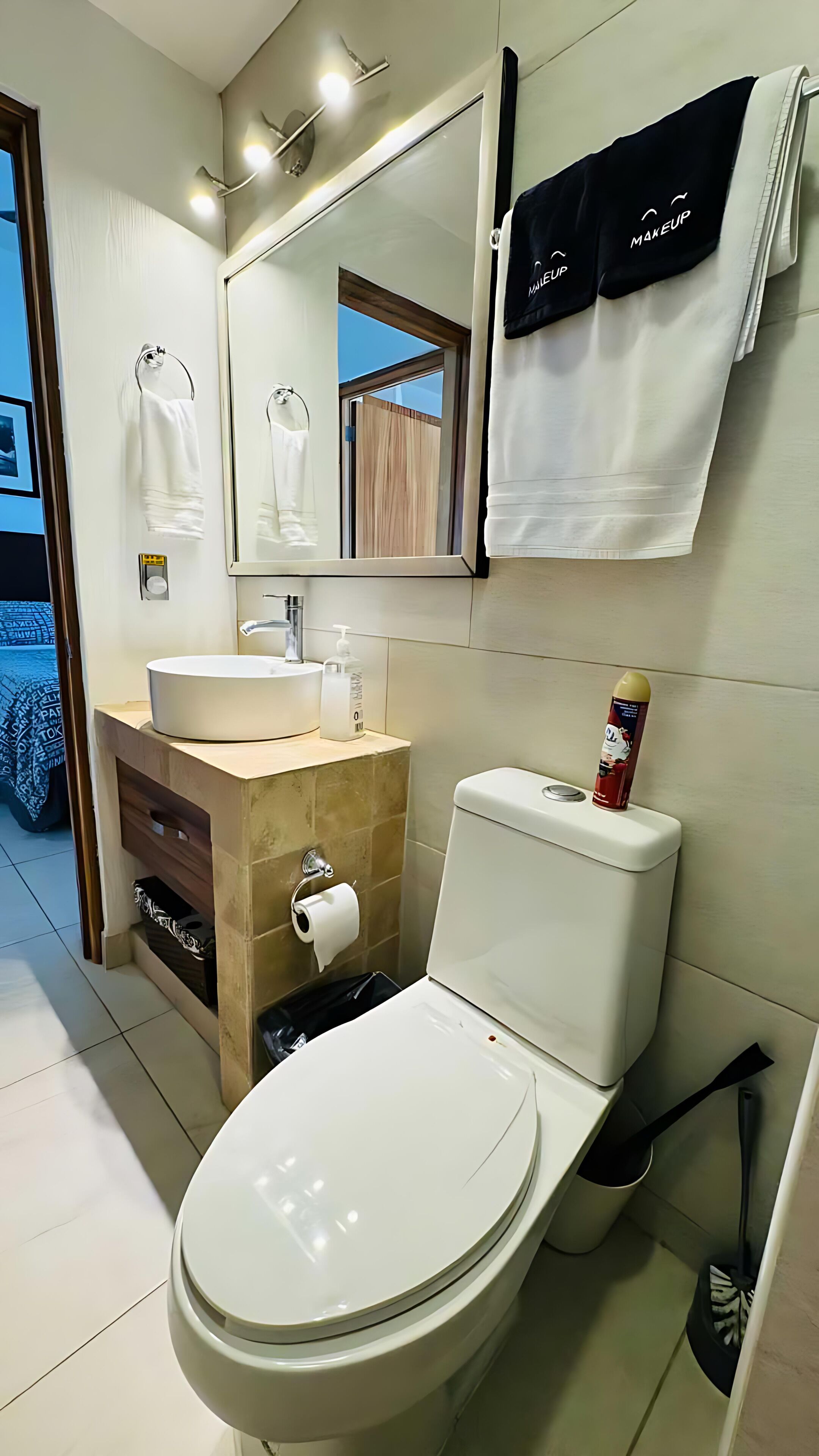 A modern bathroom with a toilet, sink, and mirror. There are towels hanging on the wall and a bottle of hand soap on the sink.
