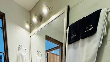 A modern bathroom with a toilet, sink, and mirror. There are towels hanging on the wall and a bottle of hand soap on the sink.
