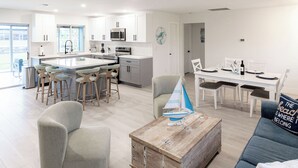 A modern kitchen with white cabinets, a central island with stools, a dining area with a white table and chairs, and a living area with a sofa and a coffee table. - Newly Remodeled 2/2 Home with Golf Access, Game Room & Salt-Water Heated Pool (Cape Coral)