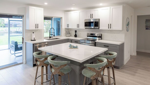 A modern kitchen with white cabinets, stainless steel appliances, and a central island with bar stools. - Newly Remodeled 2/2 Home with Golf Access, Game Room & Salt-Water Heated Pool (Cape Coral)
