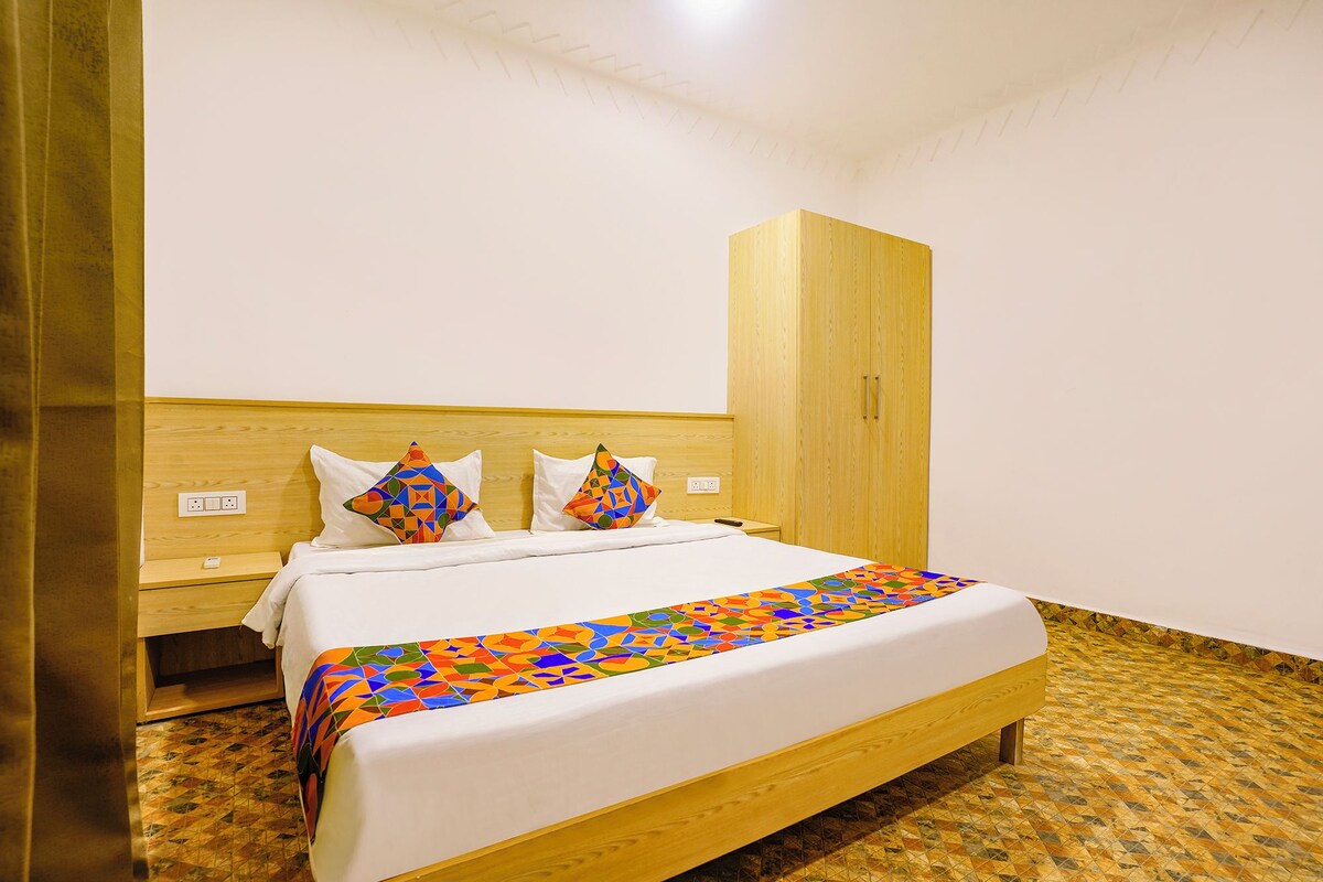 A neatly made bed with a colorful geometric-patterned bedspread, a wooden headboard, and a matching wooden wardrobe.
