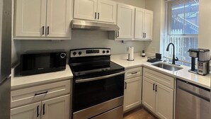 A modern kitchen with white cabinets, stainless steel appliances, and a window with blinds. - Cozy Soulard Getaway Near Downtown St. Louis (St. Louis)