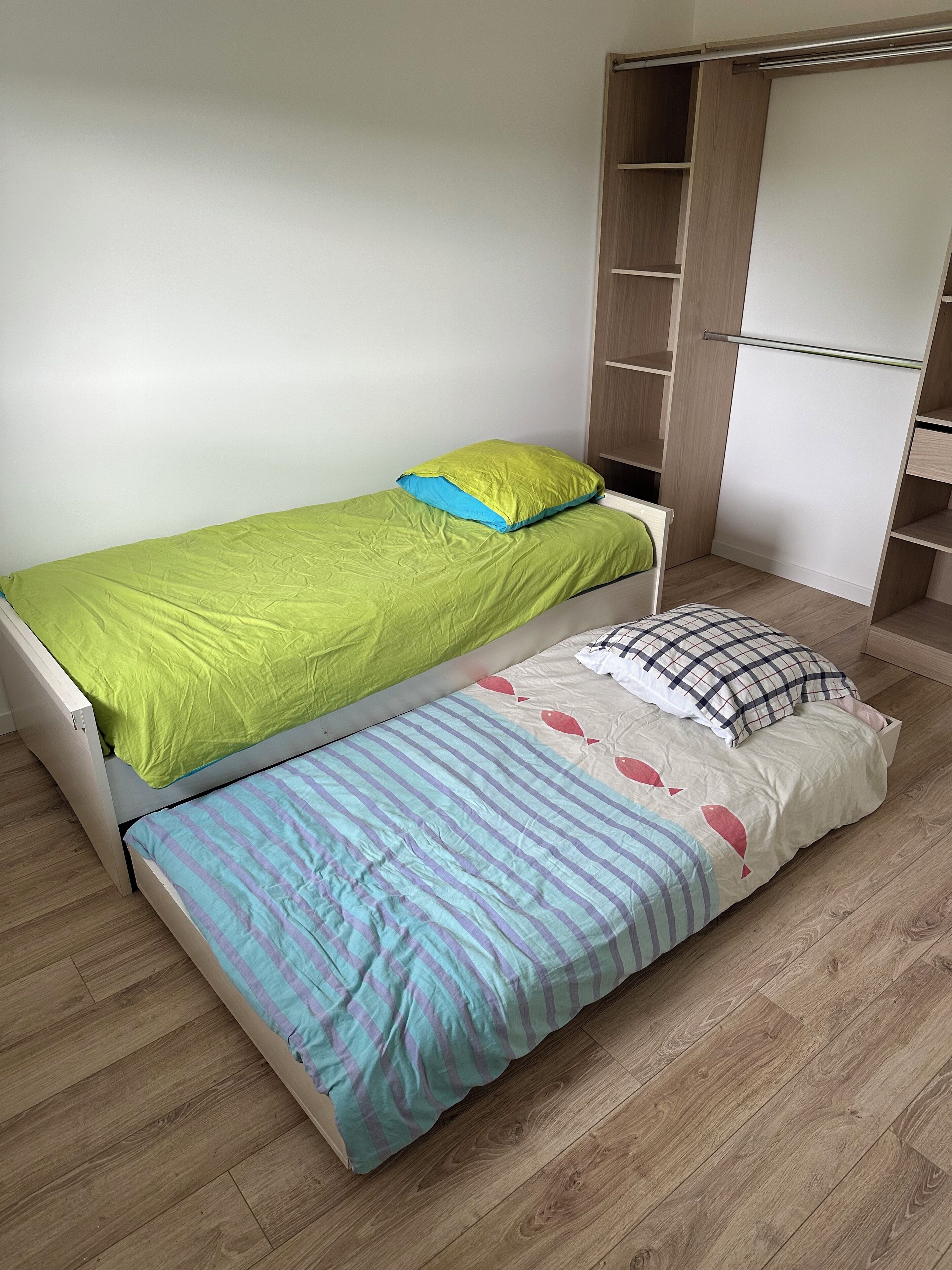 Un dormitorio con dos camas, un armario y piso de madera.