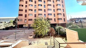 A multi-story building with a uniform facade, a central courtyard with seating, and a clear sky. - Valleca Tren Sierra Guadalupe 1 (1 bedroom apartment) (Madrid)