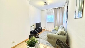 A modern living room with a sofa, a TV, a dining table with chairs, and a potted plant. - Valleca Tren Sierra Guadalupe 1 (1 bedroom apartment) (Madrid)