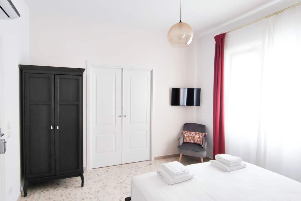 A hotel room with a bed, a wardrobe, a chair, a TV, and a window with curtains.