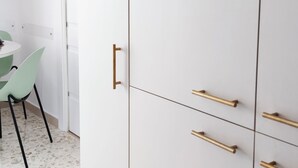 Une armoire blanche avec des poignées dorées et une chaise verte dans une pièce dont le sol est parsemé de motifs.