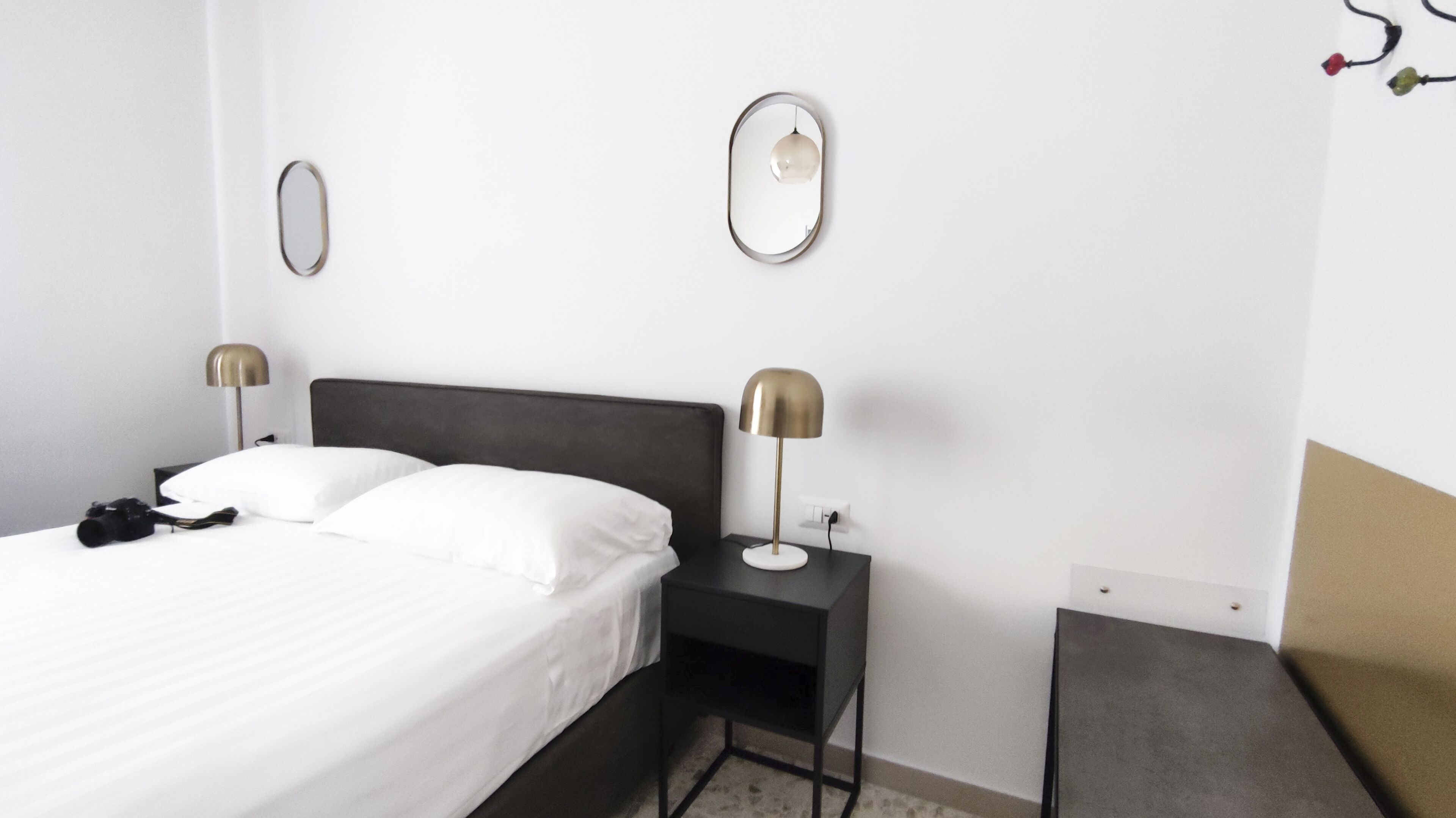 A hotel room with a bed, two bedside tables with lamps, a mirror, and a small desk.