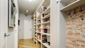 A hallway with wooden flooring, white walls, and a brick accent wall. There are white shelves with books and a white door at the end. - P&O Apartments Suligowskiego (Warsaw)