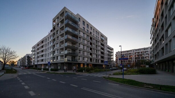Un immeuble résidentiel à plusieurs étages, doté de balcons, avec un passage piéton et un ciel dégagé.