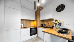 Una cocina moderna con armarios blancos, una pared decorativa de madera, horno empotrado, cafetera y un reloj en la pared.