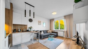 Un salon moderne avec un canapé, une table basse et un coin repas comprenant une table et des chaises. Une fenêtre avec des rideaux offre une vue sur la verdure à l’extérieur.