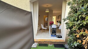 Pieni, suljettu patio, jossa on keinonurmi, valkoinen tuoli, pöytä ja punainen matkalaukku.