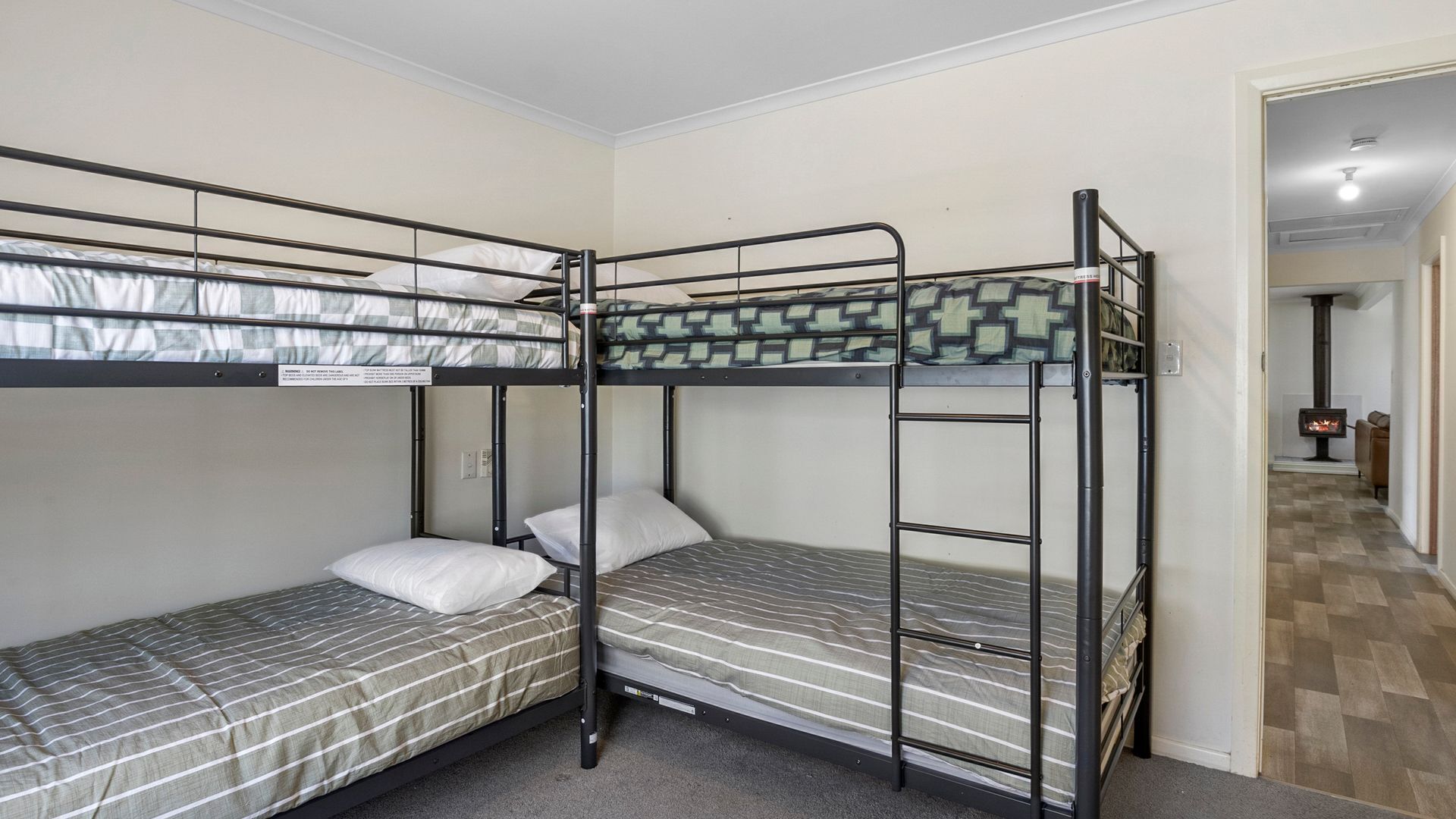 Een slaapzaal met twee bedden, een houten vloer en een zichtbare open haard in de aangrenzende kamer.