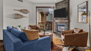 Un salon moderne avec un canapé bleu, des fauteuils marron, une cheminée en pierre et un téléviseur à écran plat fixé au mur.