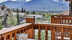 Une terrasse en bois avec un seau en métal, d’où l’on a une vue sur une ville avec ses bâtiments et, au loin, sur une chaîne de montagnes.