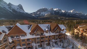 Un chalet à étages, une cour centrale avec une piscine, et un paysage enneigé avec des montagnes en arrière-plan.