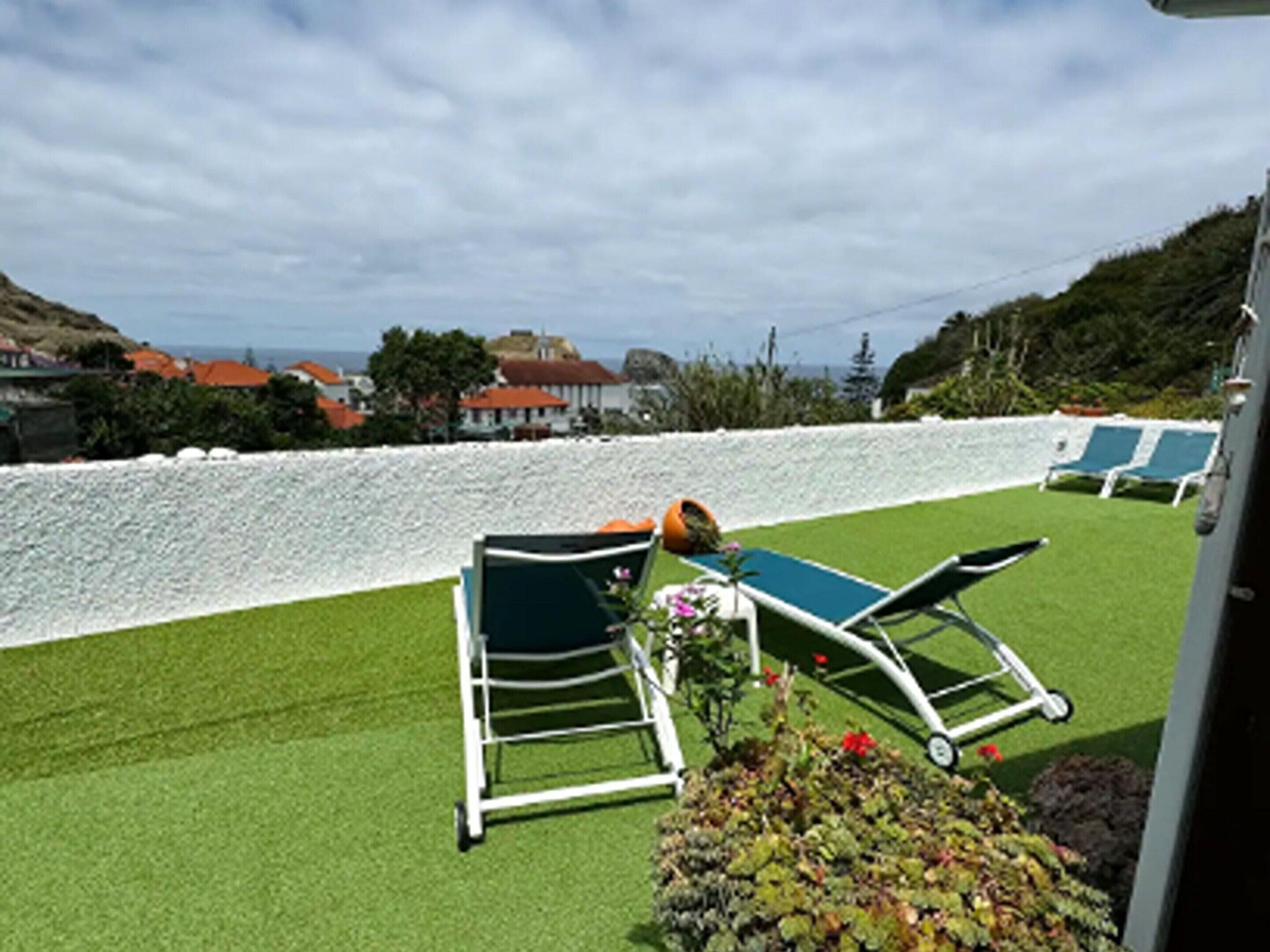 A rooftop with artificial grass, two lounge chairs, and a small garden area with flowers.