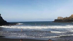 A coastal beach scene with waves, a clear sky, and rocky cliffs. - Studio in Porto da Cruz With Ocean Views (Machico)