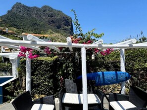Une pergola blanche ornée de fleurs roses, des meubles d’extérieur noirs et blancs, et une montagne en arrière-plan.